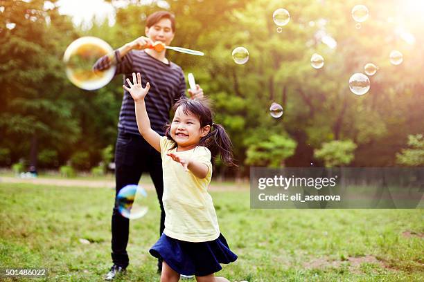father and daughter having fun in park with soap bubbles - bellenblaas stockfoto's en -beelden