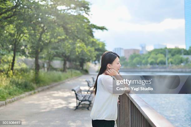 woman standing in park along the river - riverbank stock-fotos und bilder