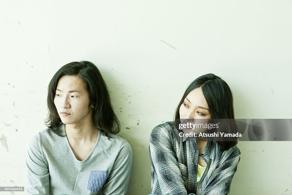 Young couple sitting against wall,looking away