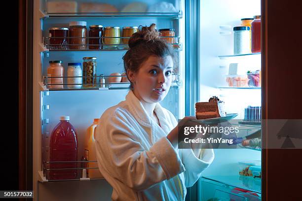 woman eating unhealthy chocolate cake in front of open refrigerator - caught in the act stock pictures, royalty-free photos & images