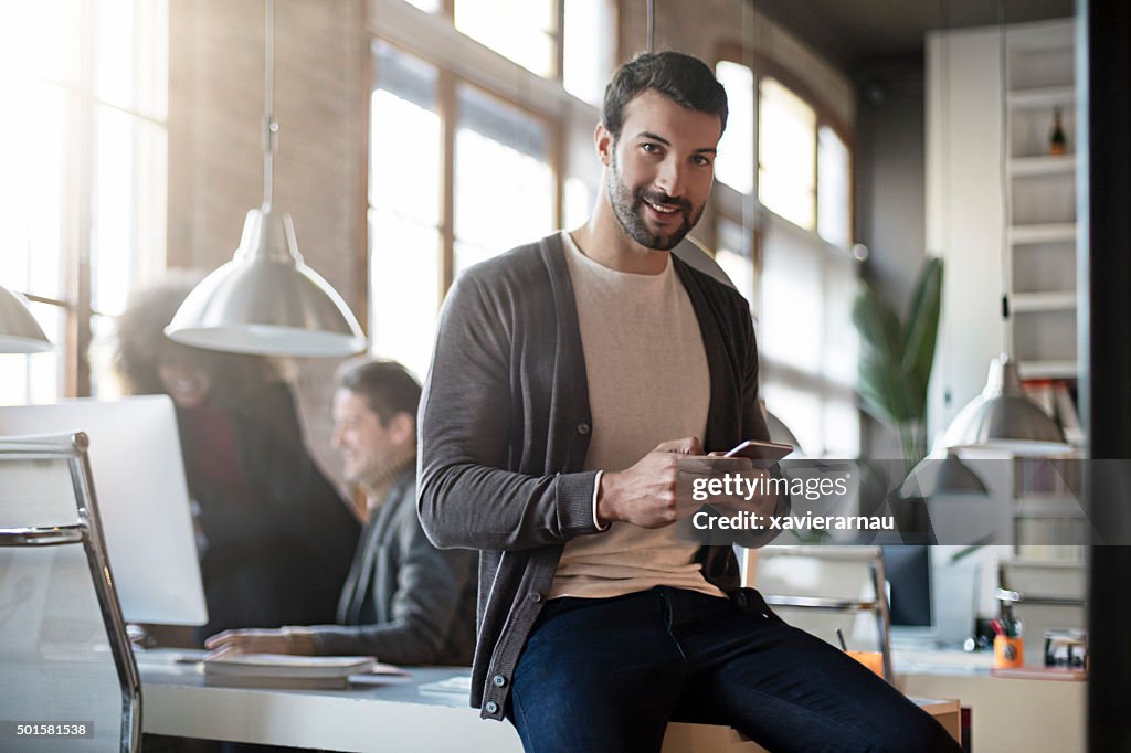 Businessman smiling with mobile phone sitting on his desk
