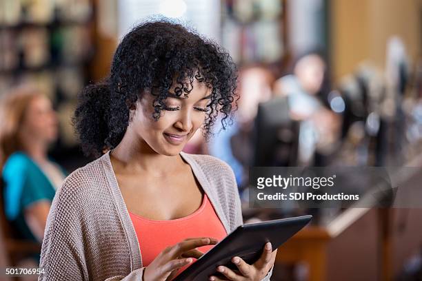african american college student uses digital tablet in modern library - cute college girl stockfoto's en -beelden