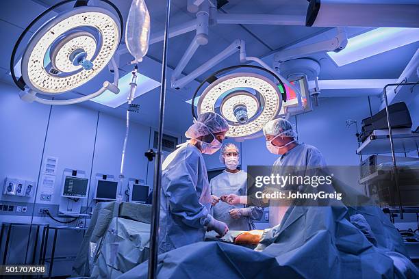 surgeons operating on patient in operating theatre under lights - doctors surgery stockfoto's en -beelden