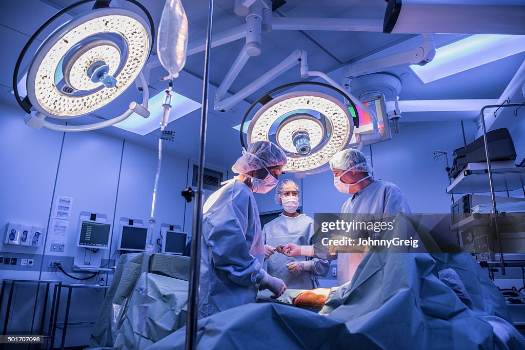 Surgeons operating on patient in operating theatre under lights