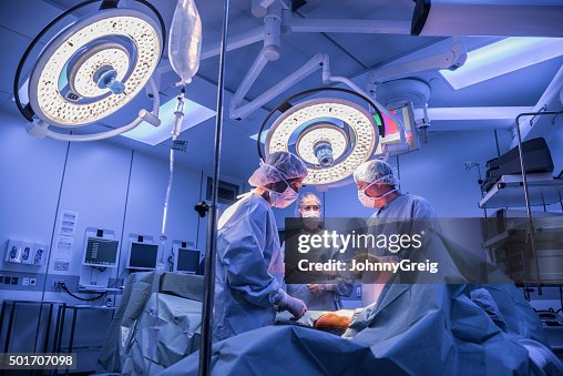 Surgeons operating on patient in operating theatre under lights Surgeons operating on patient in operating theatre under lights