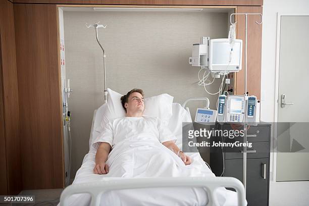 male patient lying in bed in hospital ward recovering - man in hospital stock pictures, royalty-free photos & images
