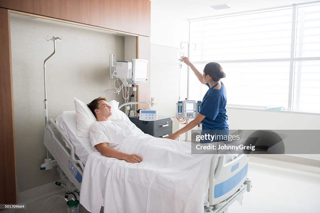 Female nurse tending to male patient in hospital bed