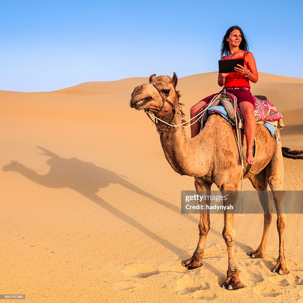 Young female tourist using digital tablet on camel, Rajasthan, India