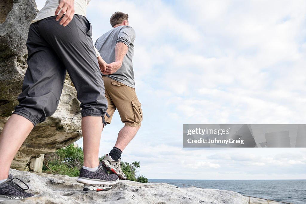 Mature couple hiking on rocks holding hands, Bondi Beach