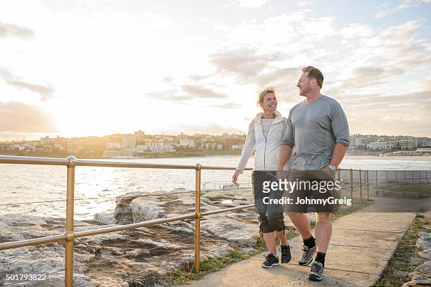 mature couple walking on boardwalk at sunset, bondi beach - boardwalk stockfoto's en -beelden