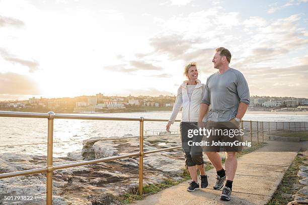 mature couple walking on boardwalk at sunset, bondi beach - sydney at dusk stock pictures, royalty-free photos & images