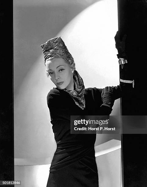 Helen Bennett wearing a long-sleeved black wool crepe dress with a wide draped belt designed by Balenciaga; and a turban made of silk, printed in a...