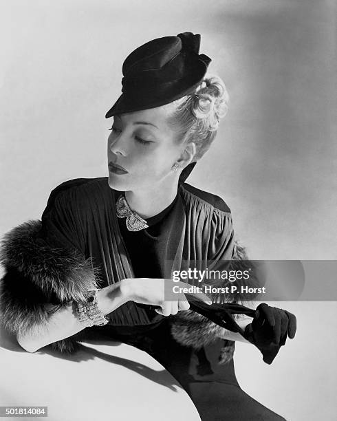 Model wearing crepe dress with multi-pleated jersey yoke, jeweled clip at throat, bracelets, fur stole, and tiny toy hat by Schiaparelli.
