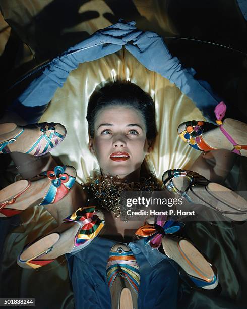 Reclining model wearing crushed-back, misty-blue evening gloves, surrounded by satin slippers in hard-candy colors.