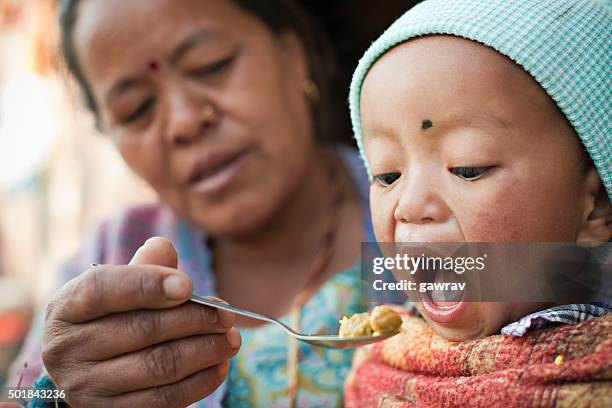 asian woman feeding food to little child. - nepal food stock pictures, royalty-free photos & images