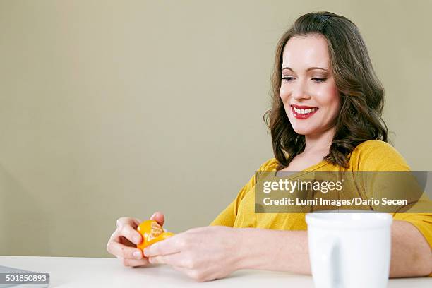 woman peeling clementine in office, munich, bavaria, germany - office snack stock-fotos und bilder