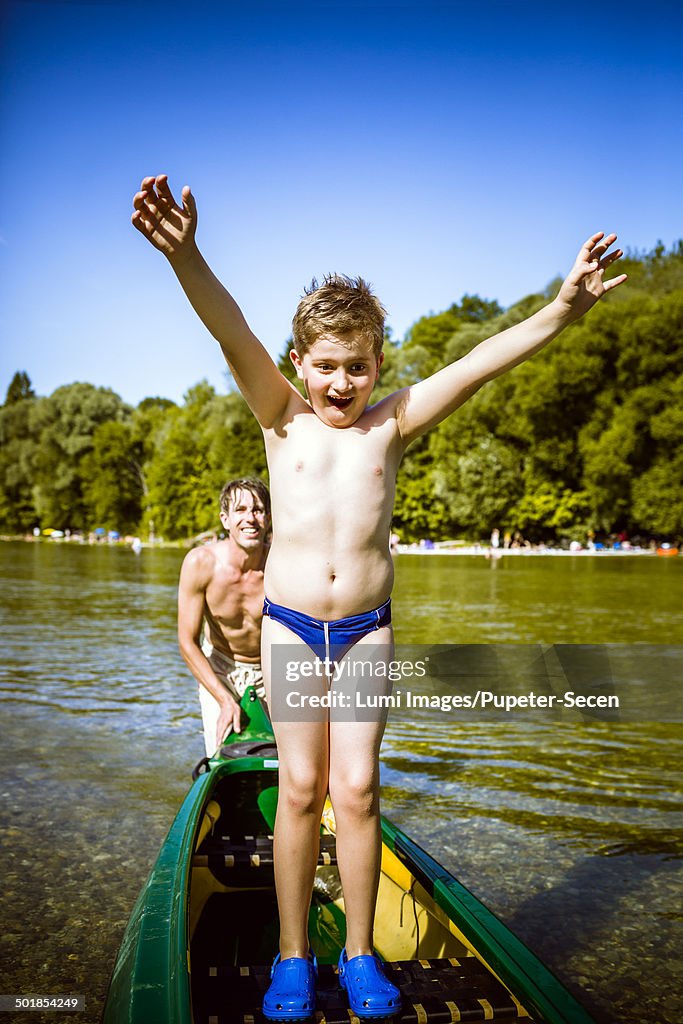 Boy in bathing trunks in a canoe, arms raised, Bavaria, Germany