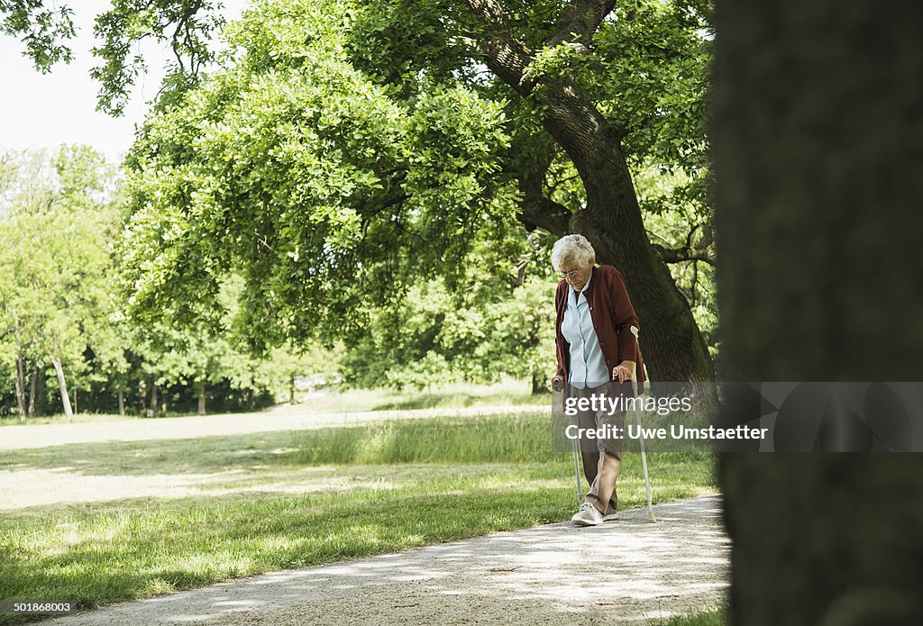 Senior woman walking through park, using walking stick