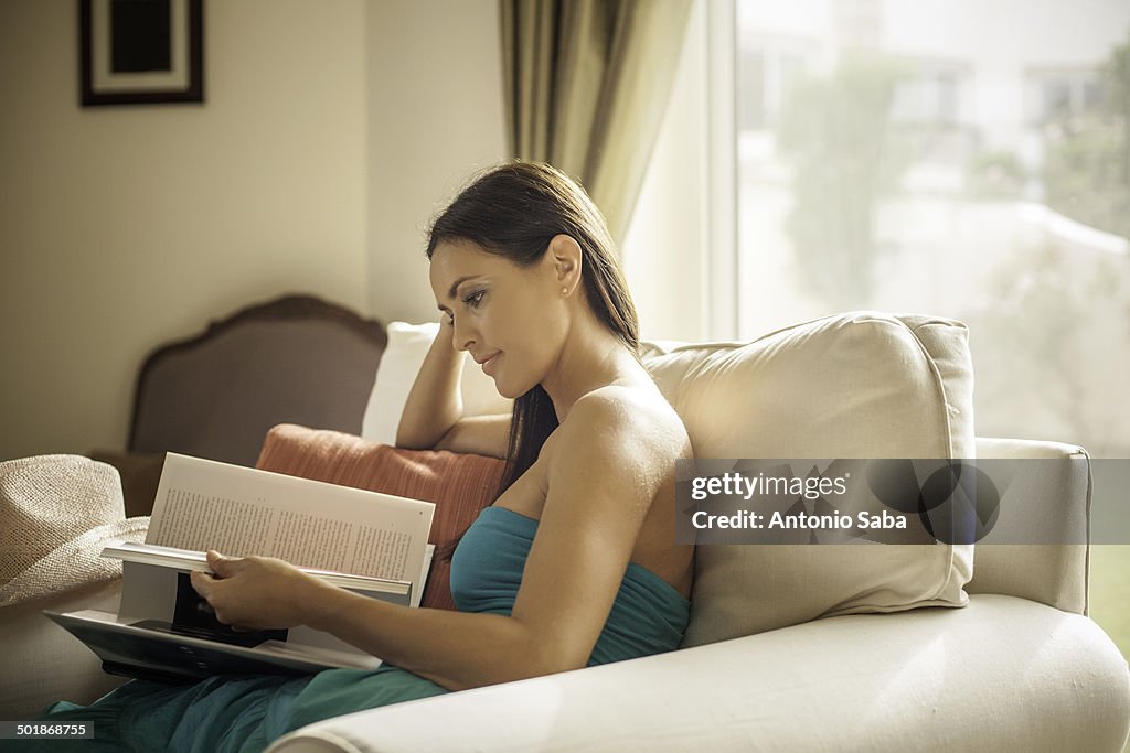 Young woman sitting in armchair reading book