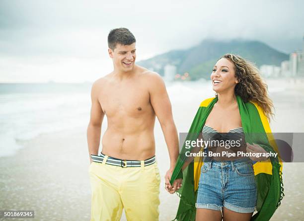 young couple strolling, woman wrapped in brazilian flag, ipanema beach, rio de janeiro, brazil - zwembroek stockfoto's en -beelden