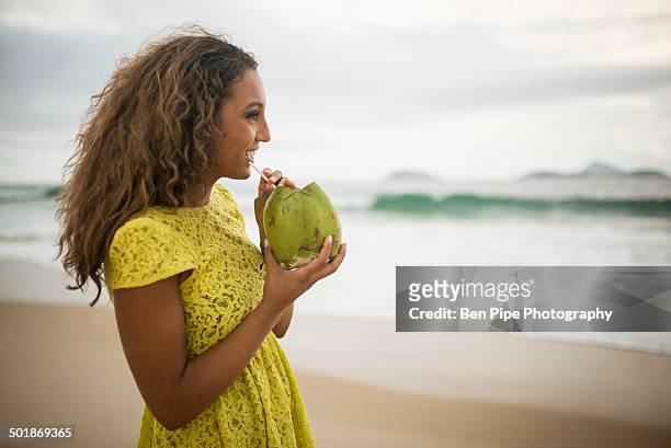 young woman drinking coconut milk on ipanema beach, rio de janeiro, brazil - ipanema beach stock pictures, royalty-free photos & images