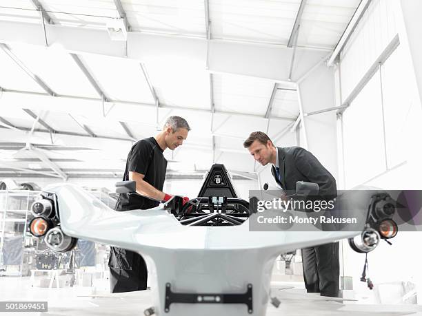 engineer and automotive designer inspecting part-built supercar in car factory - partnership teamwork build stockfoto's en -beelden