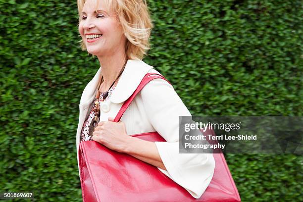 mature woman walking briskly with red shoulder bag - shoulder bag stock pictures, royalty-free photos & images