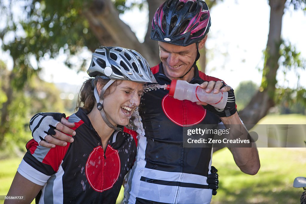 Male cyclist squirting water at woman's face