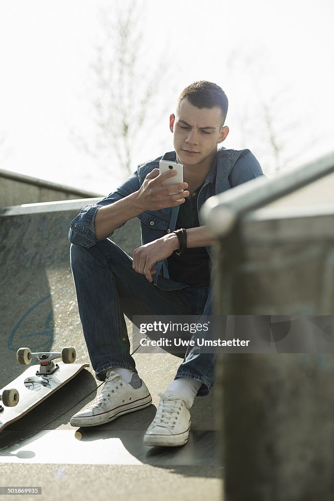 Skateboarder sitting on ramp, using smartphone