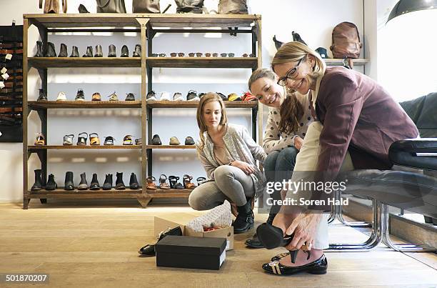 three generation females trying out shoes in shoe shop - schoenenwinkel stockfoto's en -beelden