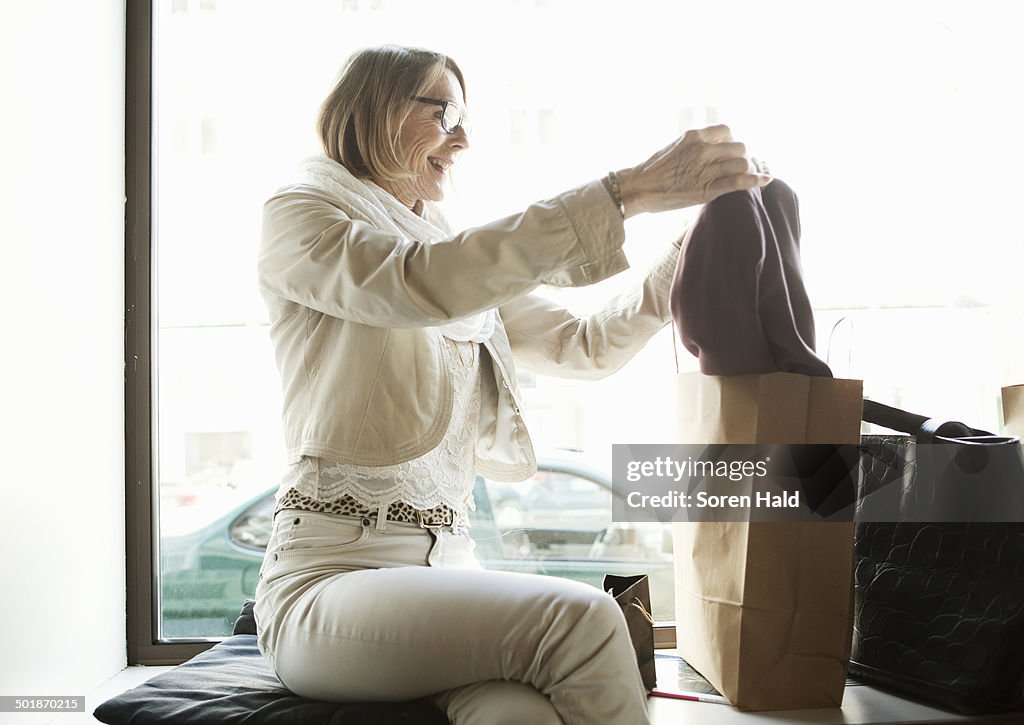 Senior woman admiring purchases in shop window seat