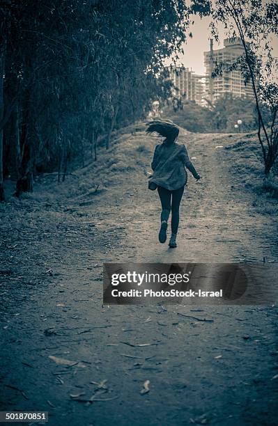 young woman running from danger up dirt track toward apartment blocks - runaway stock pictures, royalty-free photos & images