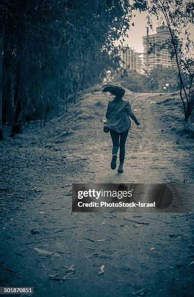 young woman running from danger up dirt track toward apartment blocks - saída imagens e fotografias de stock