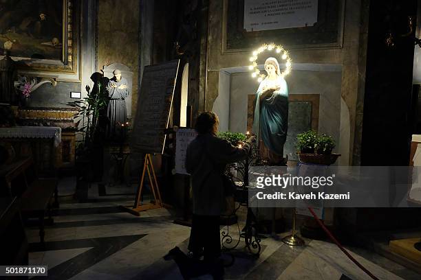 Woman lights a candle in front of an illuminated statue of the Virgin Mary in the low lit Trastevere church of Santa Dorotea on October 15, 2015 in...