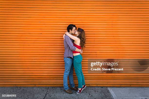 romantic couple kissing in front of orange shutter - man side standing stock-fotos und bilder