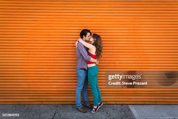 romantic couple kissing in front of orange shutter - couple standing full length stock pictures, royalty-free photos & images
