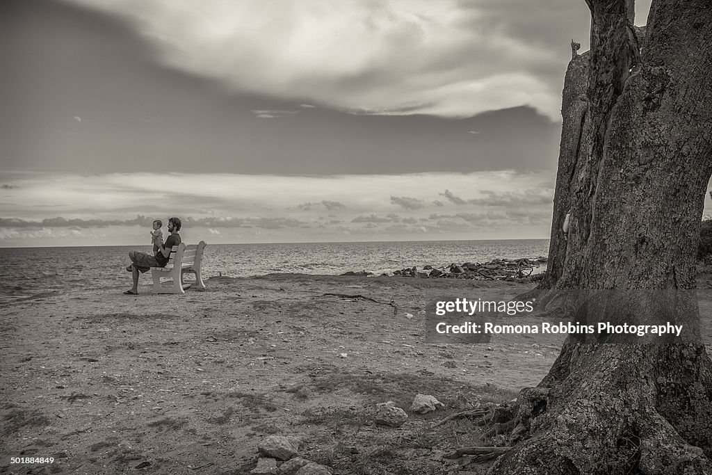 Black and white image of father and toddler daughter on beach bench