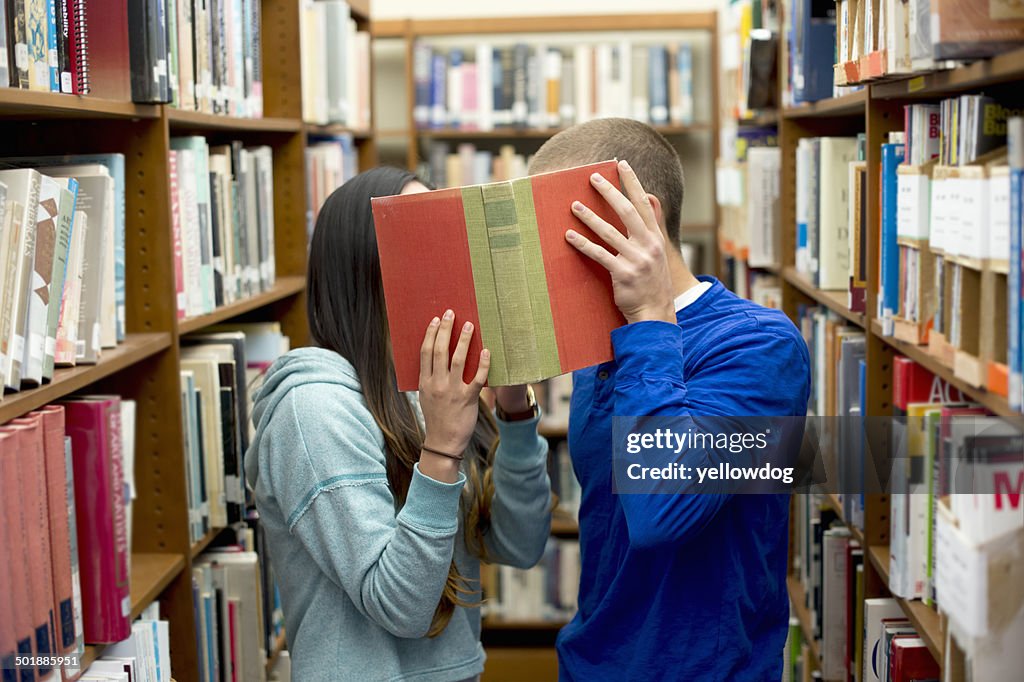 Young couple hiding behind book