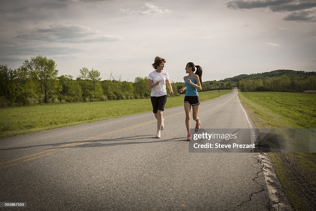 Mid adult woman and teenage girl running on road