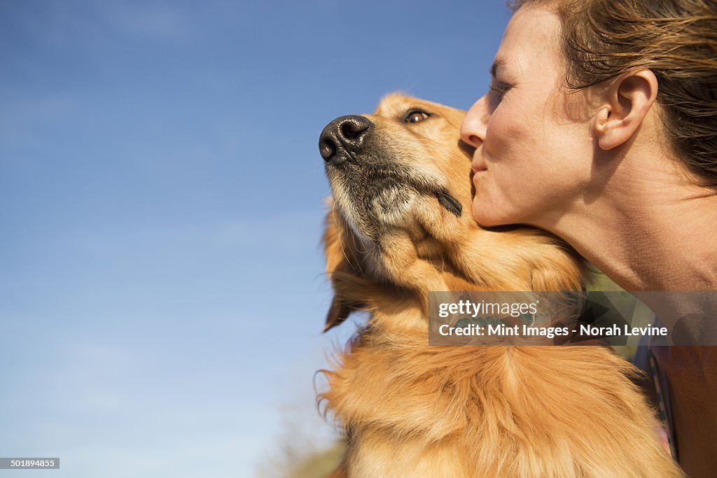 A woman kissing a pet dog on the cheek.