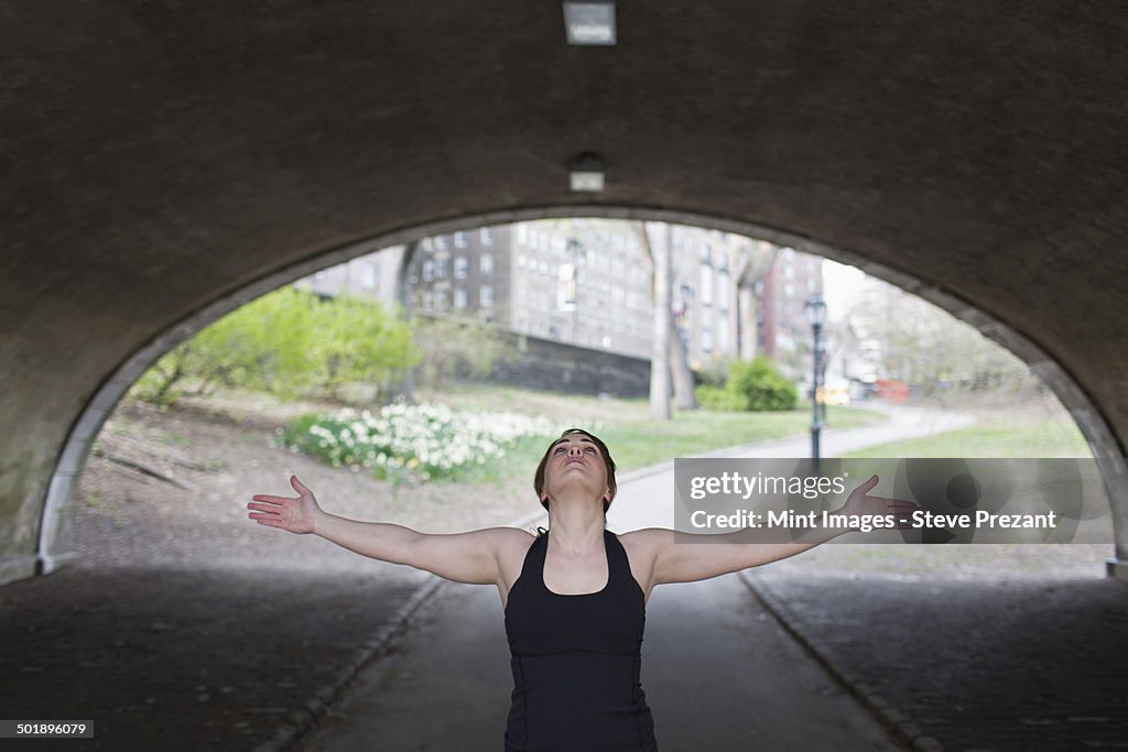 A woman in Central Park, in a black leotard and leggings, doing yoga.