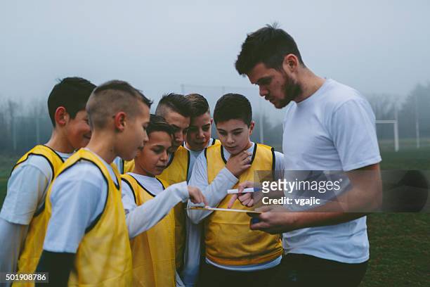 coach giving instruction to his kids soccer team. - football coach stock pictures, royalty-free photos & images