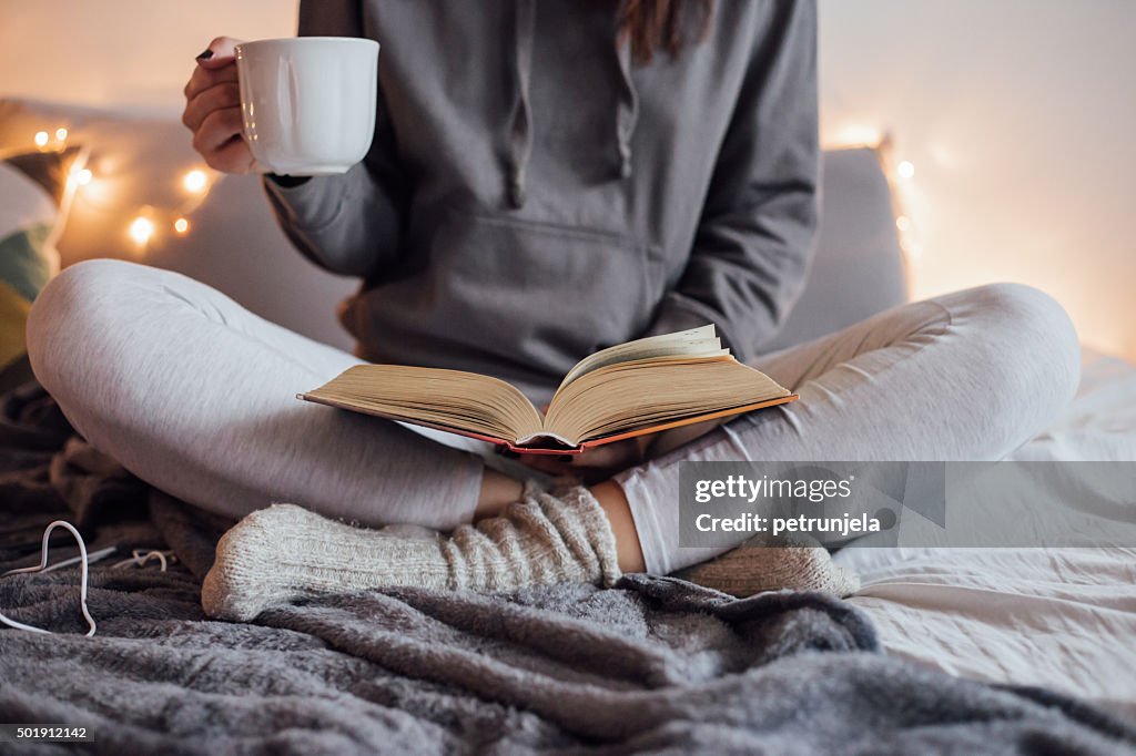 Girl drinking hot tea and reading book in bed