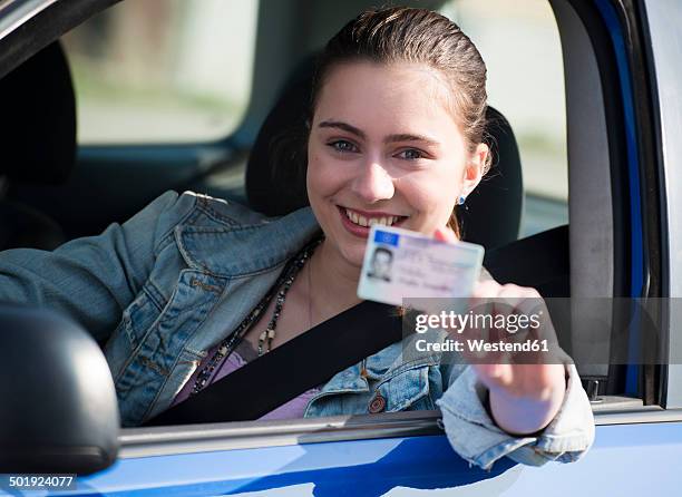 smiling teenage girl sitting in car showing driving license, partial view - licence stock-fotos und bilder