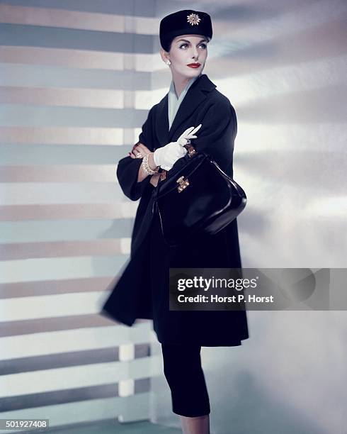 Model wearing blue coat by Jablow, with hat by Dior New Look, holding Gucci bag, and David Webb jewelry.