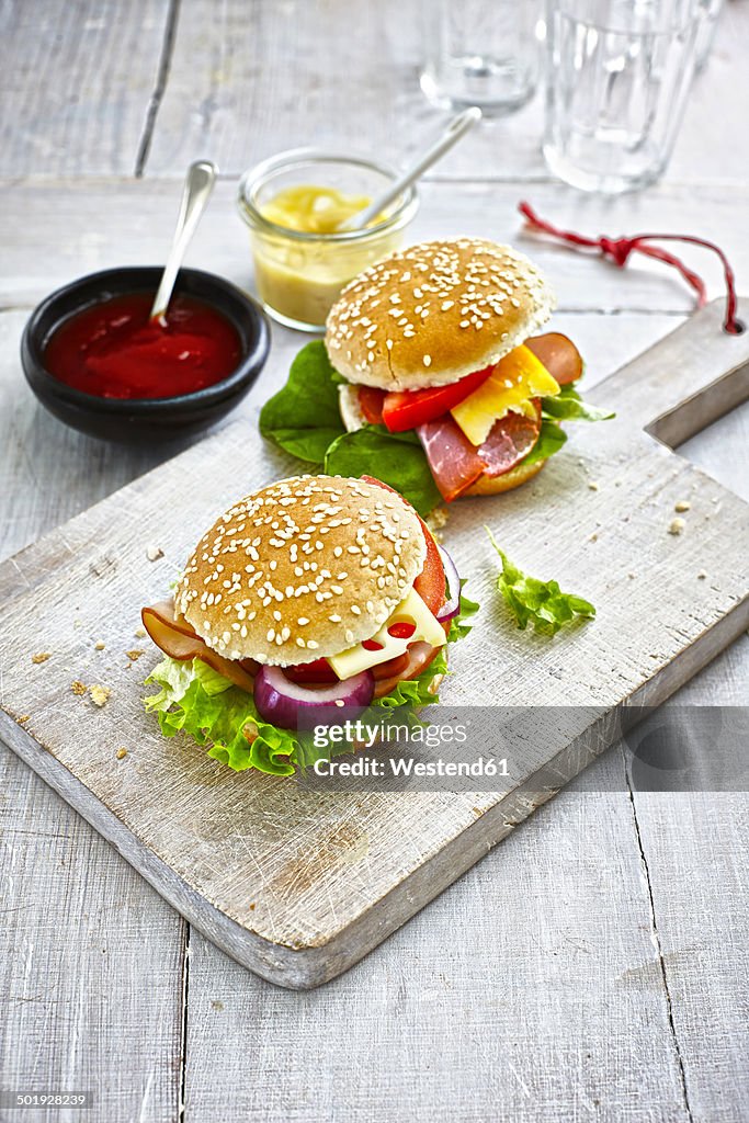Two prepared burgers, mustard and ketchup on wooden ground