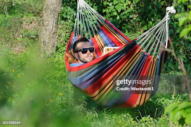 germany, young man lying in hammock and reading a magazine - nature magazine 個照片及圖片檔