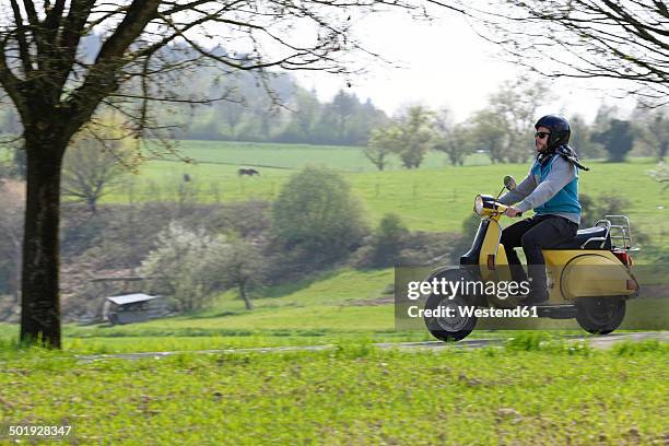 young man driving with his vespa on country road - roller fahren stock-fotos und bilder