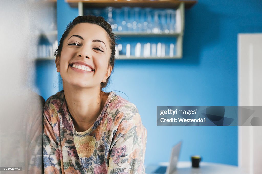 Portrait of happy young woman leaning against fridge in her kitchen