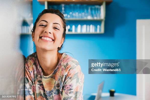 portrait of happy young woman leaning against fridge in her kitchen - blu chiaro foto e immagini stock